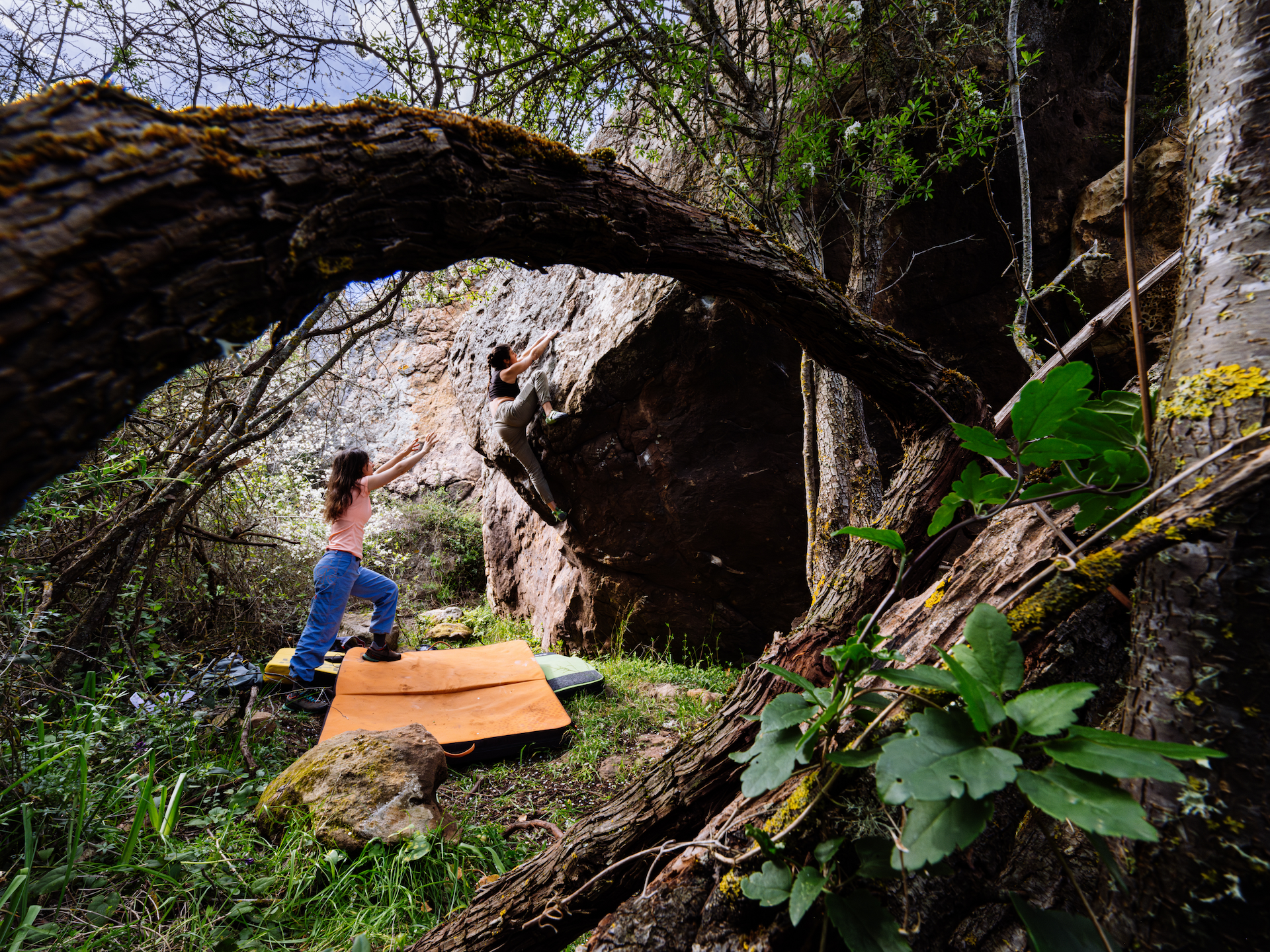 Two female climbers at Arkham bouldering spot in action, one climbing and the other spotting